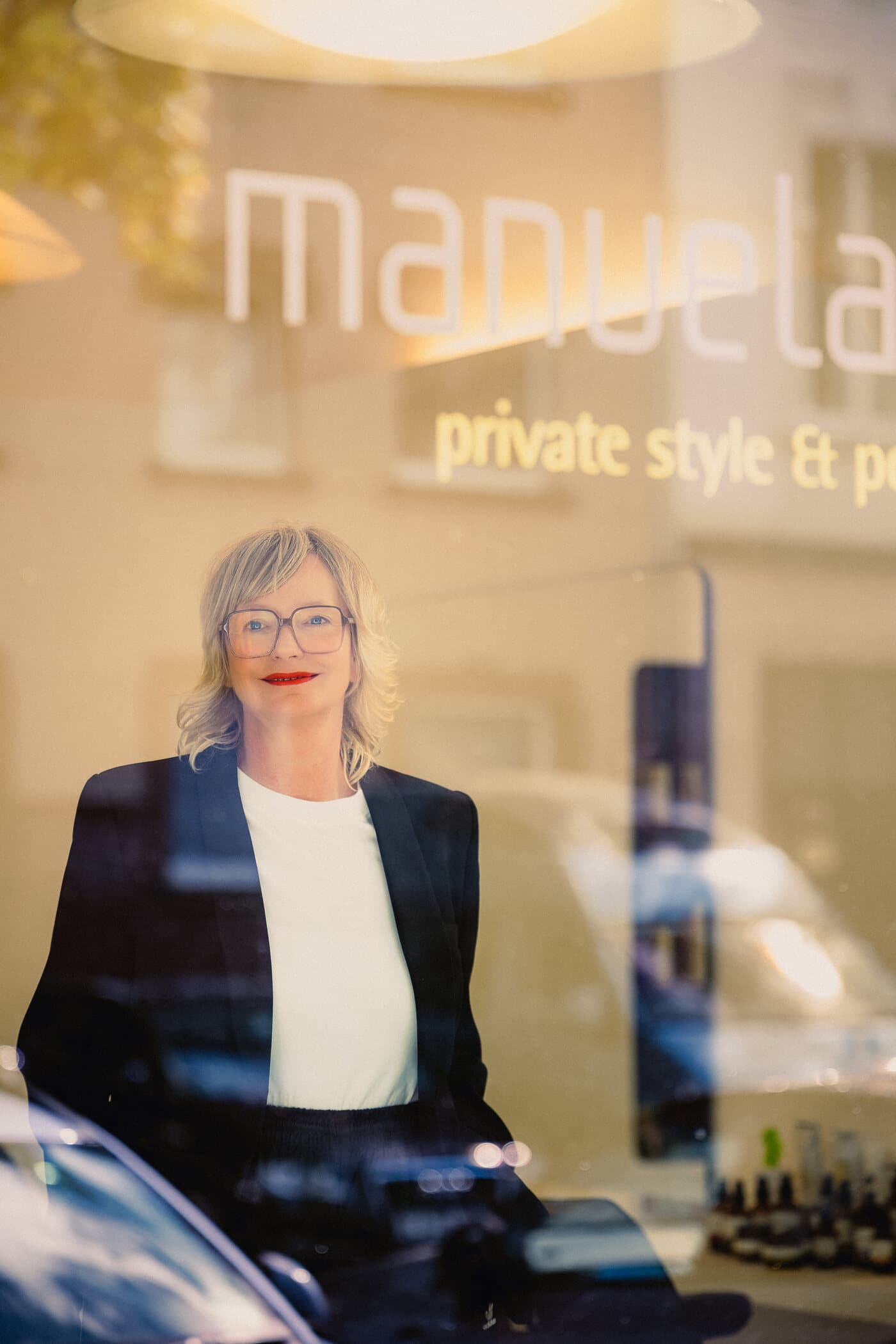 Manuela hinter ihrem Schaufenster, die Straße spiegelt sich im Glas