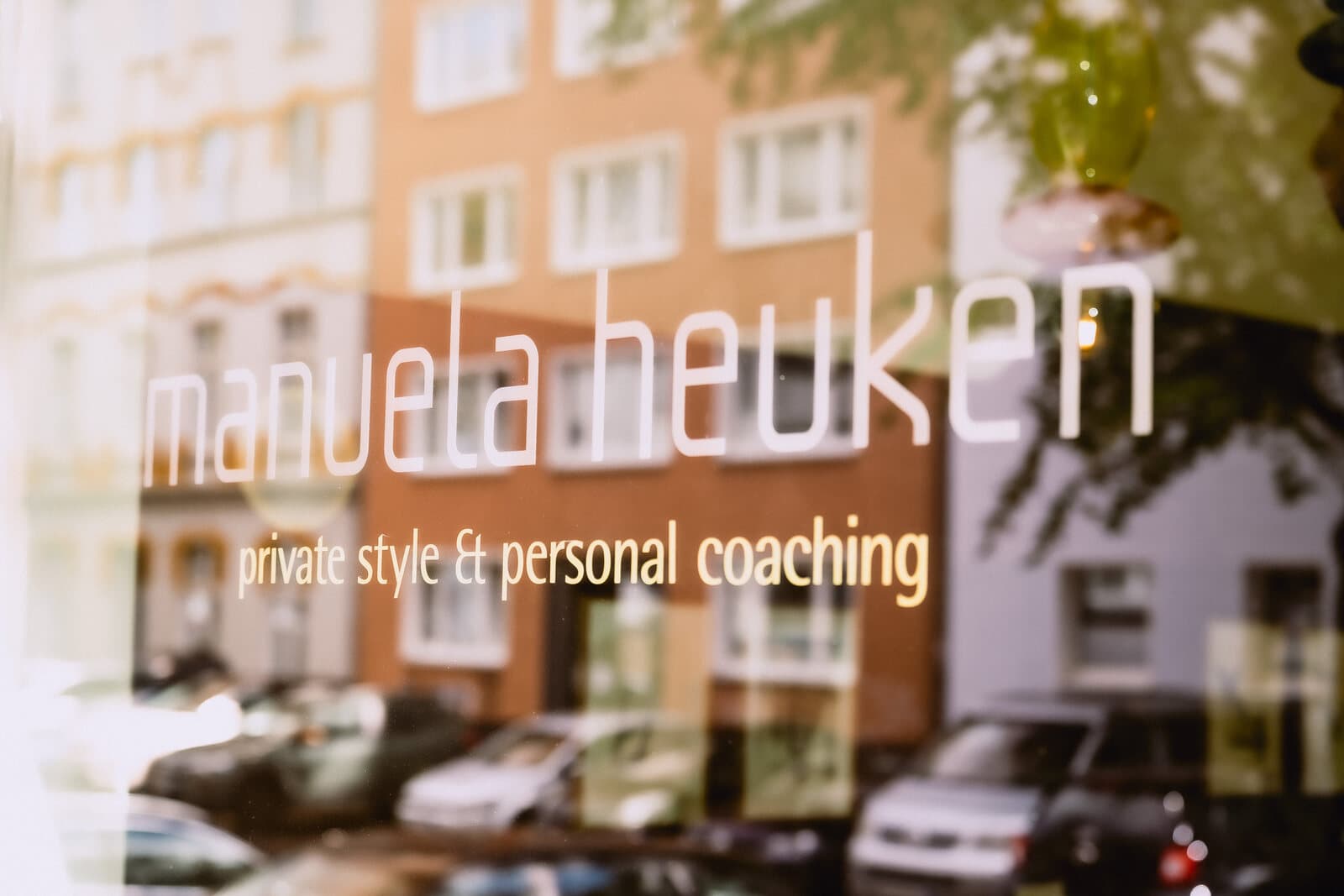 Die Wortmarke manuela heuken im Schaufenster, die Straße spiegelt sich